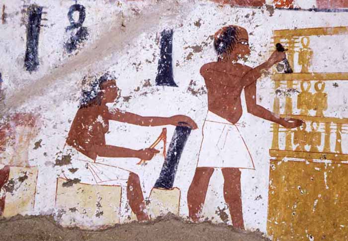 Detail - Worker uses adze to rough out a column of blackwood for a Djed amulet. These objects are associated with Osiris, the Egyptian God of the afterlife and their design is meant to represent the vertebral column.